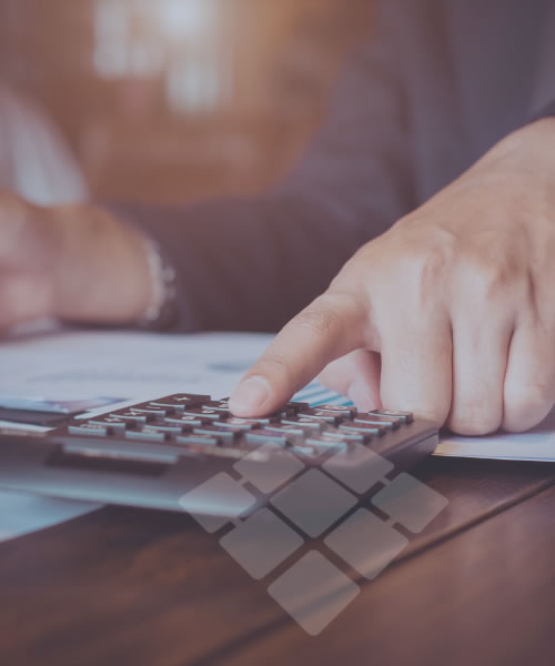 Mão de pessoa usando calculadora sobre uma mesa de trabalho, com foco em atividades financeiras