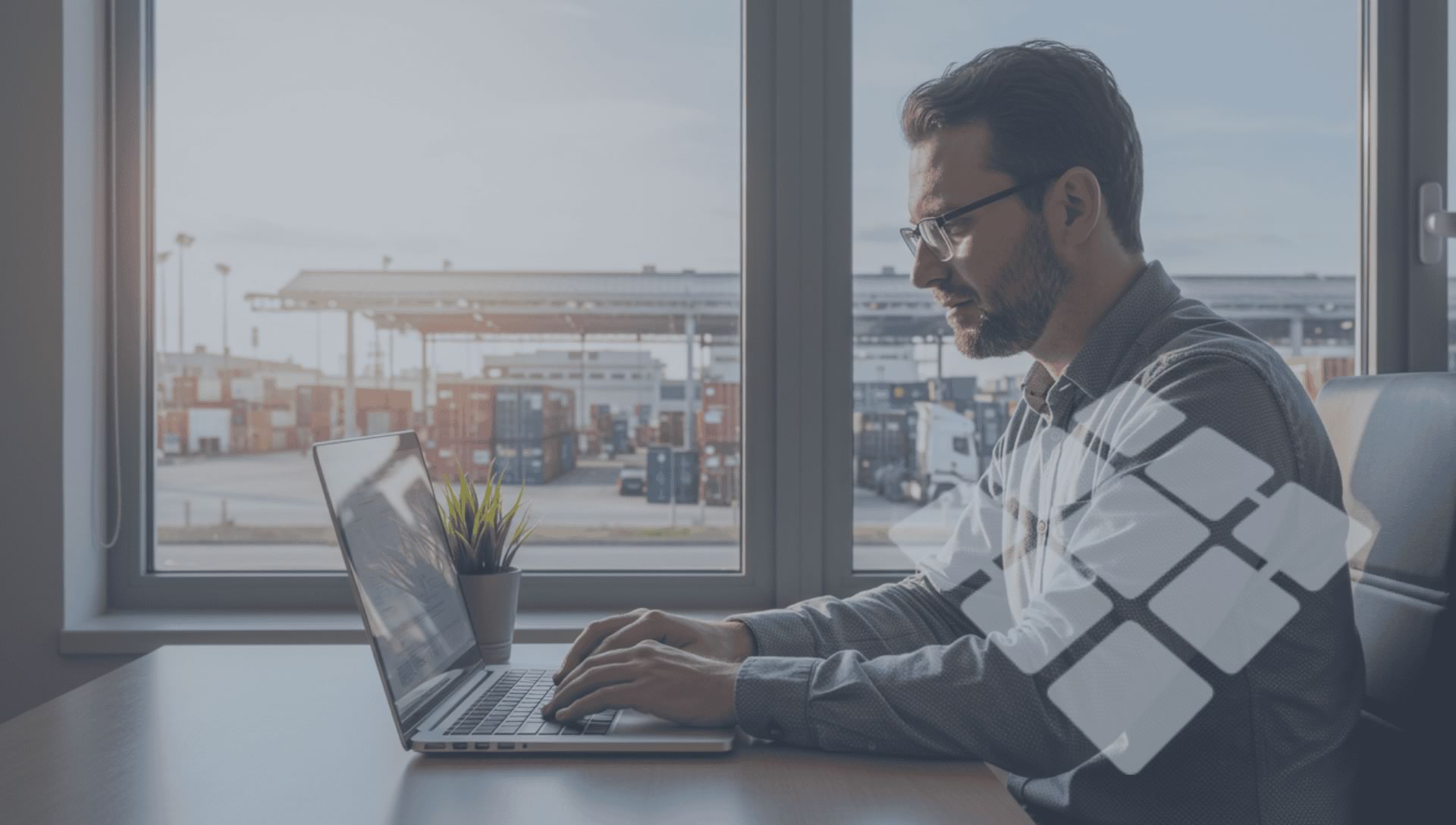 Freight forwarder analisando operações logísticas em notebook, com pátio de carga ao fundo repleto de caminhões estacionados.