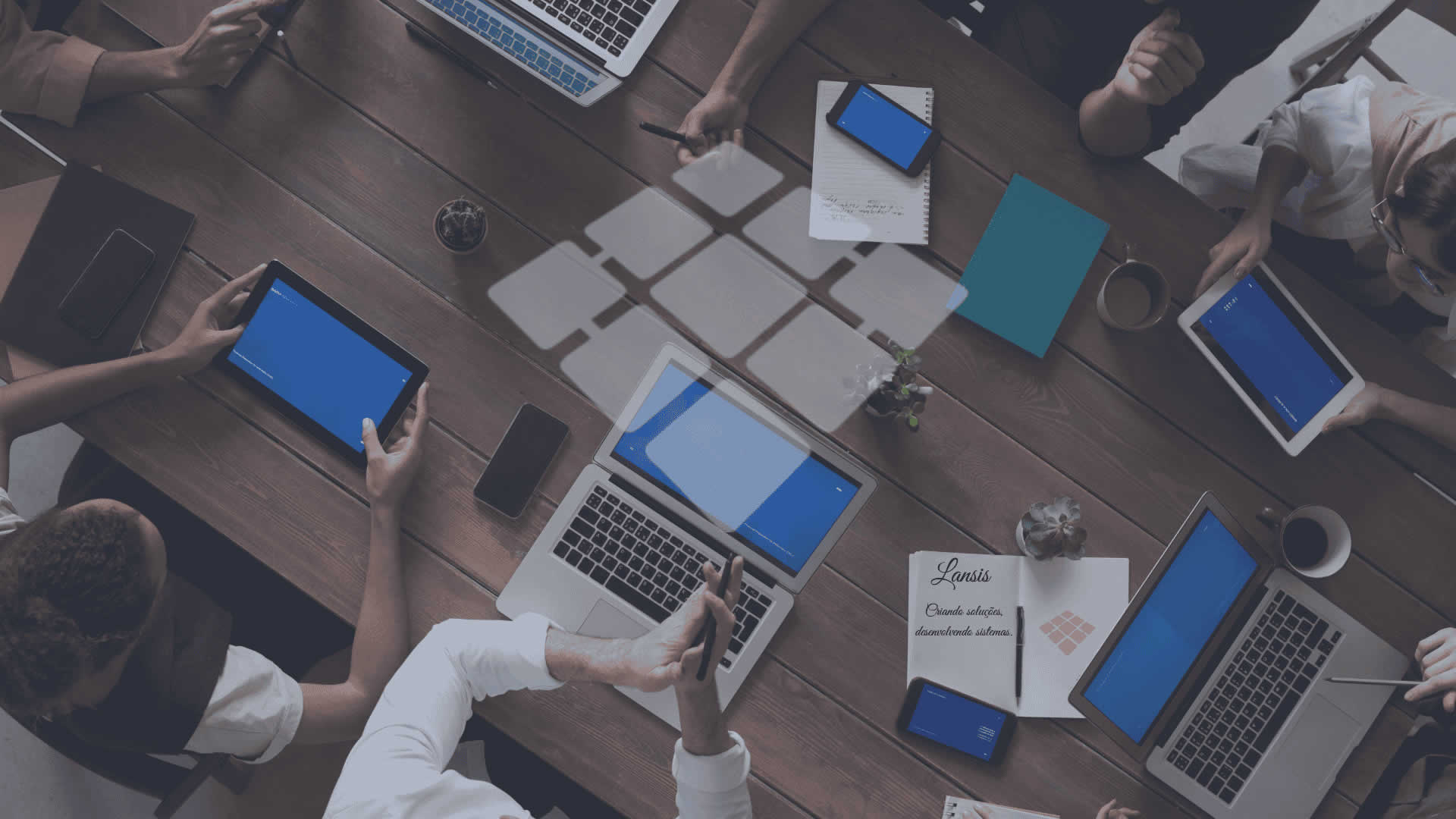 Equipe reunida em mesa de trabalho com computadores, representando colaboração e tecnologia — seção 'Sobre Nós'